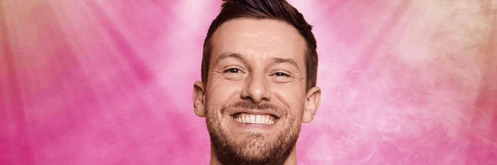 Chris Ramsey in front of a pink background.